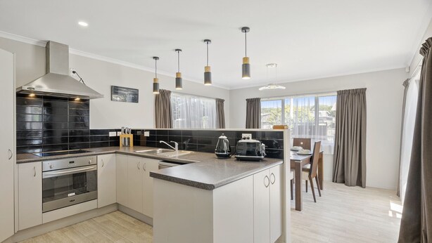Une cuisine moderne dotée d’un îlot central, d’appareils électroménagers en acier inoxydable et de luminaires suspendus.