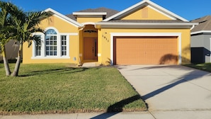 A single-story house with a yellow exterior, a brown garage door, and a well-maintained lawn. - Magical Family Friendly Pool and Lake House (Kissimmee)