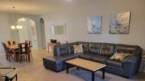 A living room with a sectional sofa, a coffee table, and a dining area with a table and chairs. - Magical Family Friendly Pool and Lake House (Kissimmee)