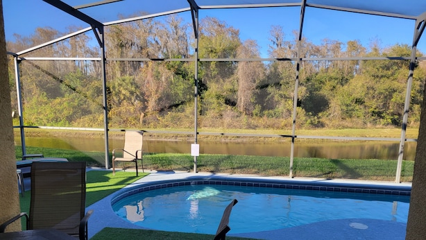 A pool area with a view of a lake, surrounded by trees and a covered patio with chairs and a table. - Magical Family Friendly Pool and Lake House (Kissimmee)
