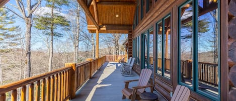 Relax on the deck with Adirondack chairs and a bench, surrounded by trees and a clear sky.