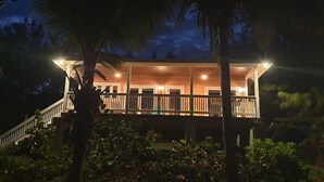 A two-story building with a balcony, surrounded by palm trees and vegetation. - Eve's Cottage - Ocean Breeze Peaceful Getaway (Governor's Harbour)