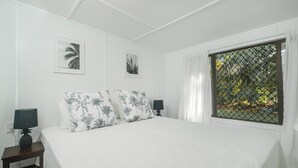 Una camera da letto con un letto grande, due comodini, una finestra vista verde e due quadri appesi al muro.