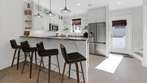A modern kitchen with white cabinetry, stainless steel appliances, and a central island with bar stools. - Stunning 4BR 3BA. Pool. Gym. Pets Welcome. 0.7 mi to beach access (Santa Rosa Beach)