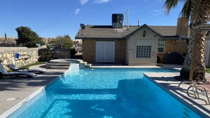 Ein rechteckiger Swimmingpool mit klarem, blauem Wasser, umgeben von einer Steinmauer und einem kleinen Backsteinhaus mit Garage.