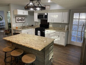 A kitchen with granite countertops, white cabinets, a stainless steel stove, and a large island with bar stools. - STYLISH & FUN on El Paso's Eastside (El Paso)