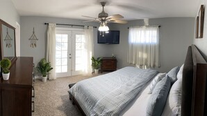 Ein Schlafzimmer mit einem Bett, einem Deckenventilator, einem Fernseher und einer Tür, die auf einen Balkon führt.