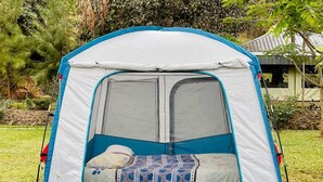 A portable tent with a sleeping area inside, set up on grass with trees and a building in the background. - Jangwani Camp Sagana (Murang'a)