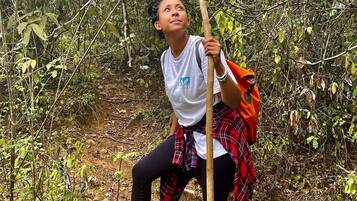 Uma pessoa caminhando em uma área florestada com vegetação densa e uma trilha de terra.