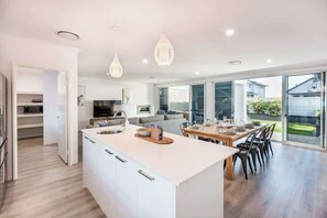 A modern kitchen with a central island, dining area with chairs, and large sliding glass doors leading to a backyard.