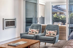 A modern living room with two grey armchairs, a wooden coffee table, and a wicker sofa.