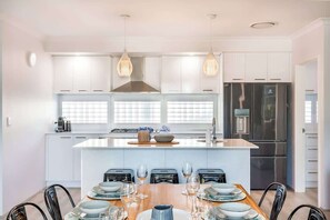A modern kitchen with white cabinetry, a central island with seating, stainless steel appliances, and pendant lighting.