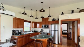 Eine Küche mit Holzausstattung, einem Edelstahlkühlschrank, einer Mikrowelle und einer Kaffeemaschine. Es gibt einen Esstisch aus Holz mit Stühlen und einen Barhocker.