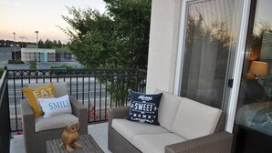 Un área de estar al aire libre con mobiliario de mimbre, incluyendo un sofá y dos sillones, cada uno con cojines decorativos.