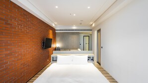 A modern hotel room with a brick wall, a large bed, a flat-screen TV, a mirror, and a wooden floor. - Formosa Yacht Resort (Tainan)