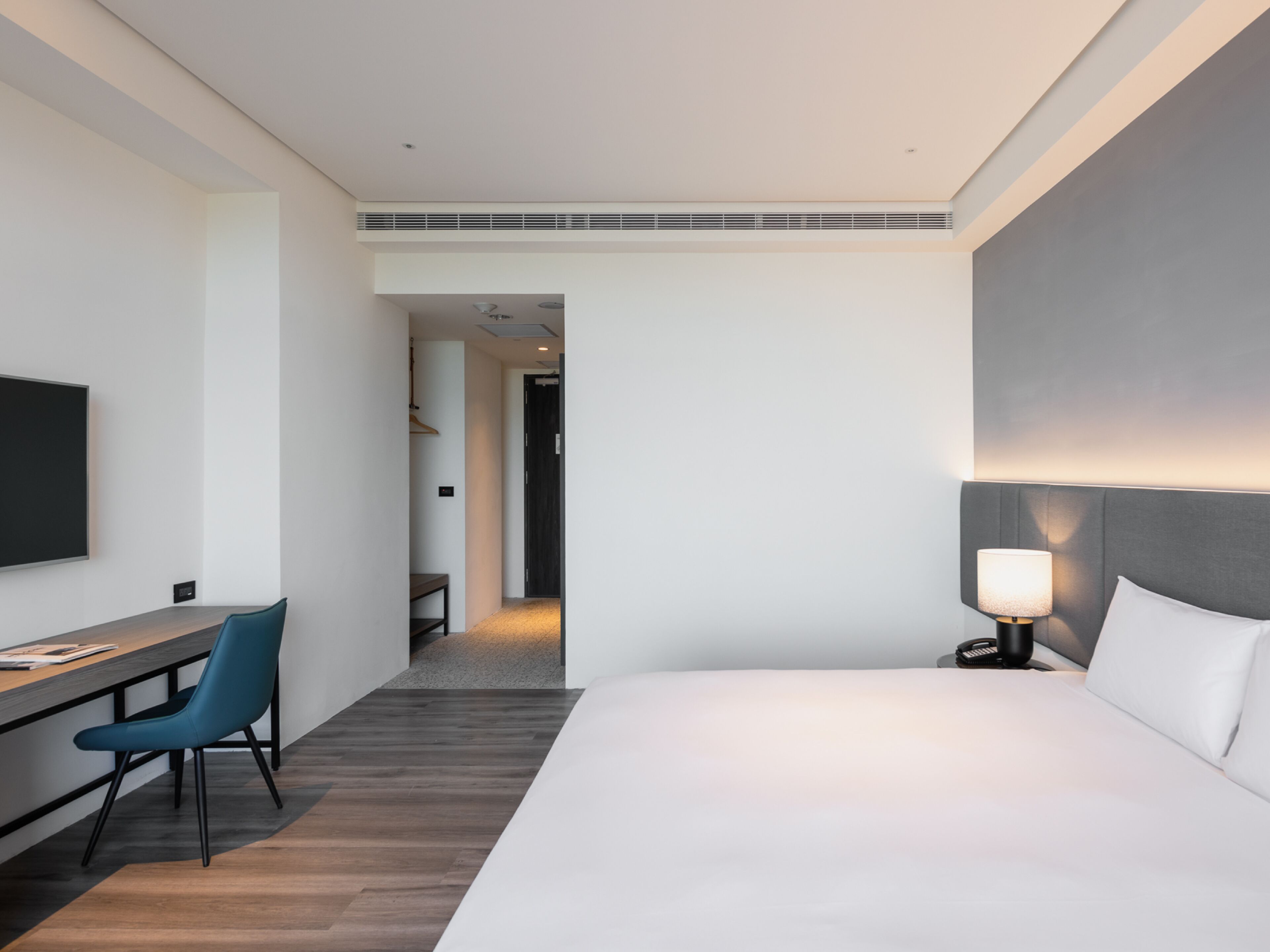 Una habitación de hotel moderna con una cama grande, un escritorio con silla, una televisión y una lámpara de noche.