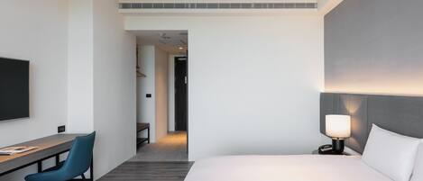 A modern hotel room with a large bed, a desk with a chair, a television, and a bedside lamp.