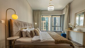 Et moderne soveværelse med en stor seng, et sengebord, en gulvlampe, en lysekrone, et vindue med udsigt til skyskrabere og et spejl på væggen.