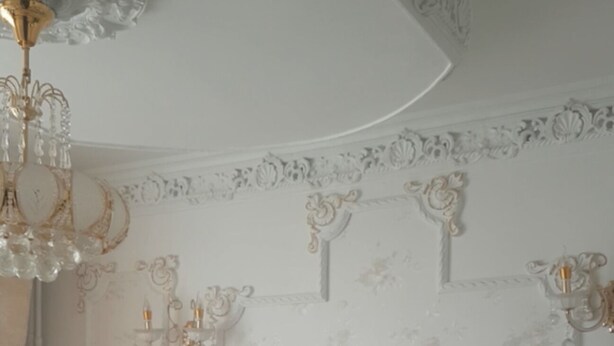 Ein Schlafzimmer mit einem großen Bett, aufwändigen Wandverzierungen und einem Chandelier.