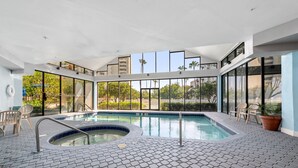 En moderne indendørs swimmingpool med glasvægge, flisegulv og udsigt til grøn vegetation udenfor.