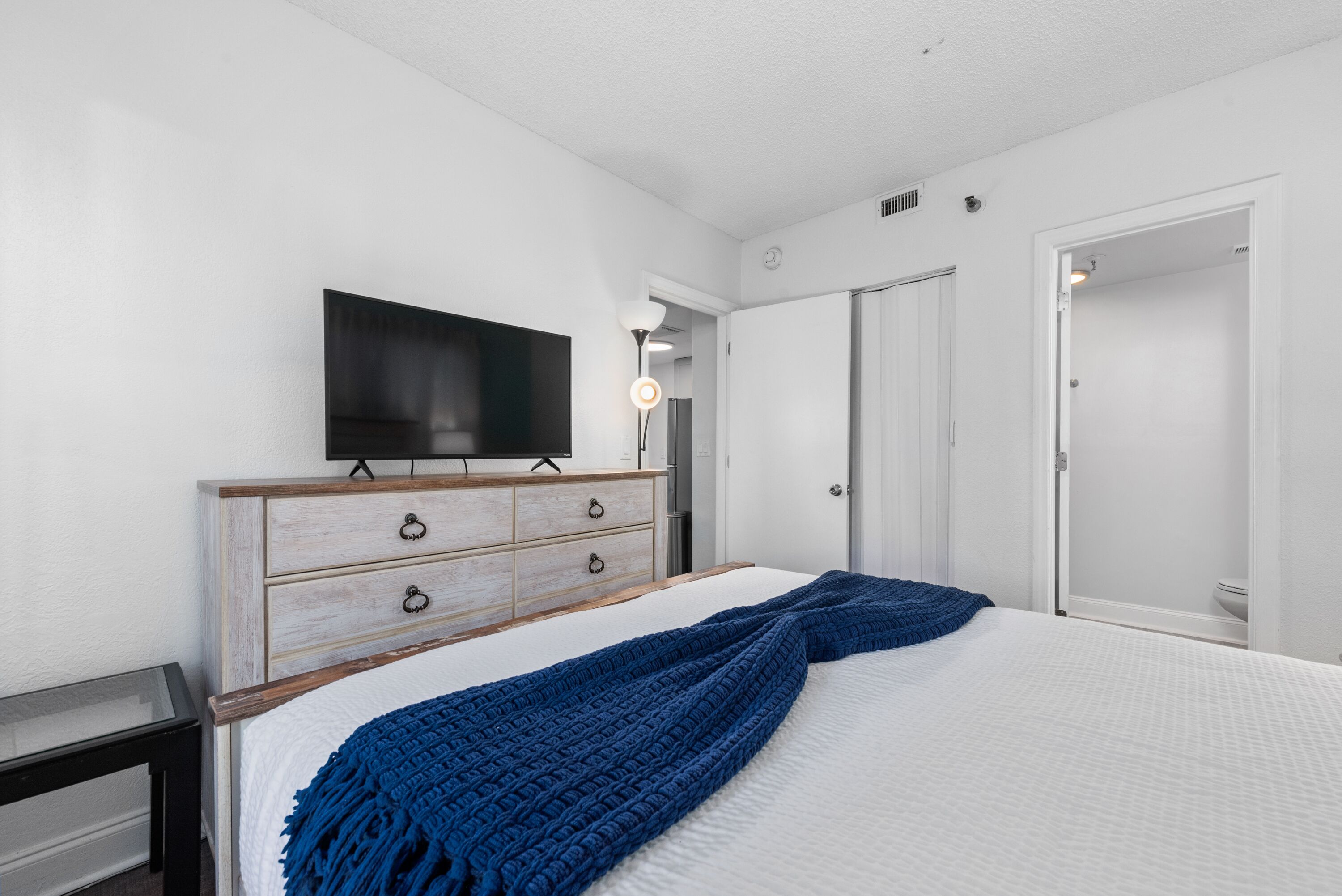 Een slaapkamer met een bed, een dressoir, een televisie en een kledingkast.
