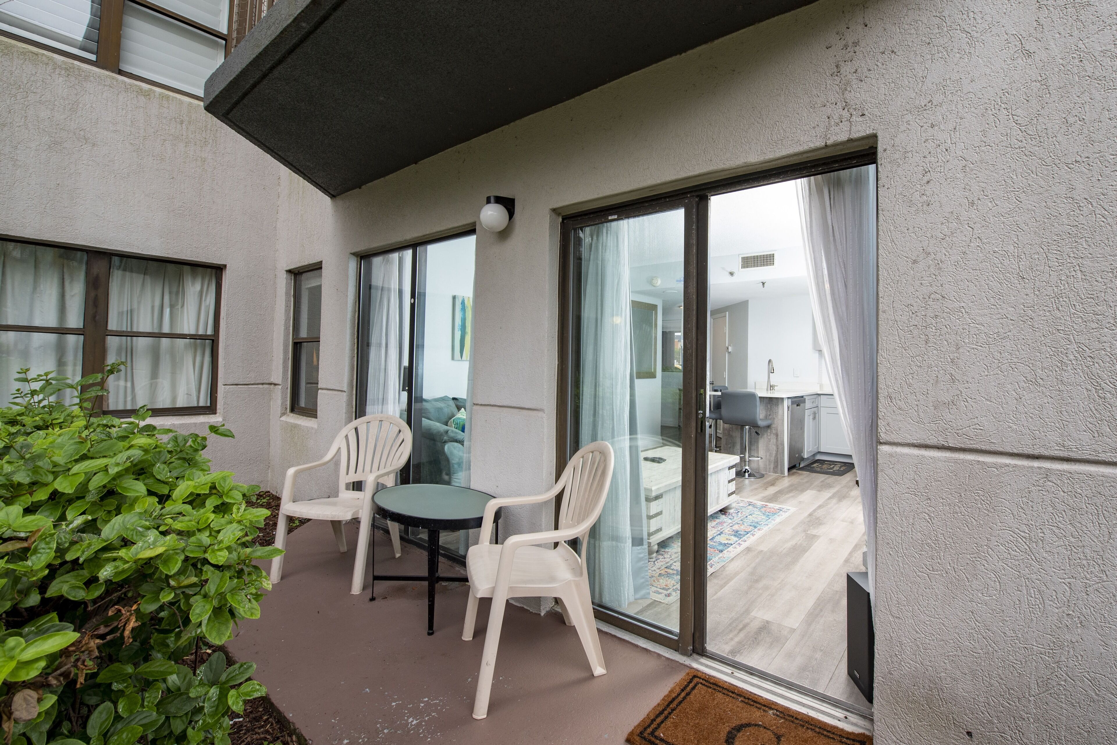 Een balkon met twee witte plastic stoelen, een kleine tafel en een plant in een pot.