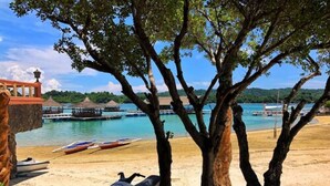 A beach with a jet ski, a boat, and a pier with buildings in the background. - Grace Island Resort by Cocotel (San Jose)