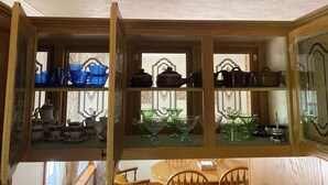 A wooden cabinet with glass doors displaying various kitchenware.