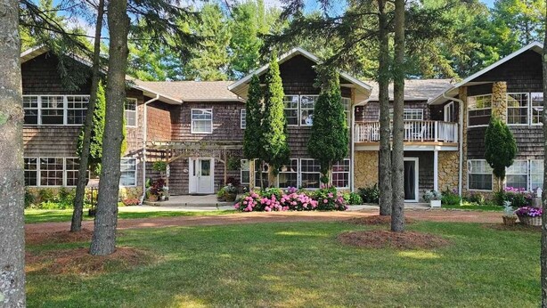 A two-story lodge with a stone facade, wooden exterior, and a front porch with a railing. - 4 bedrooms, 2 bathrooms and a three-season playroom,  Second-floor Unit. (Sturgeon Bay)