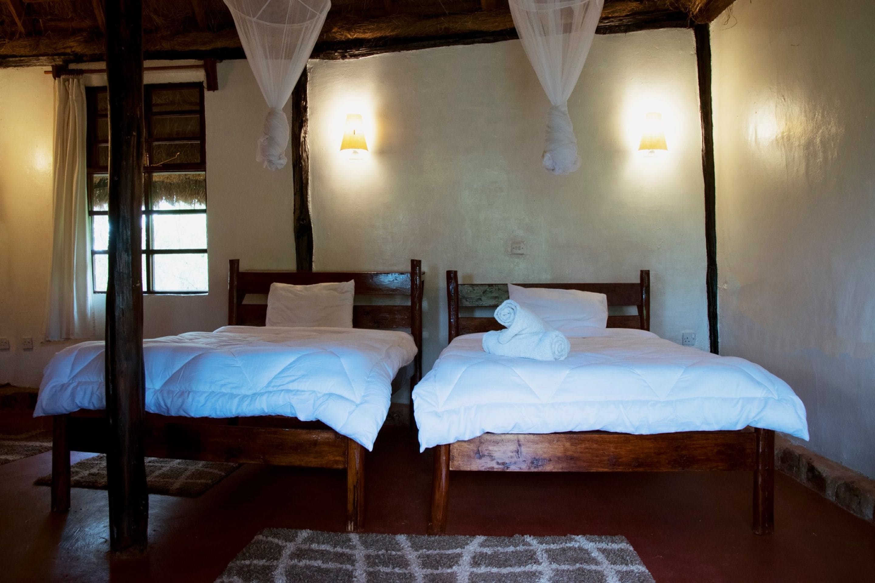 A room with two wooden beds, white bedding, and a mosquito net.