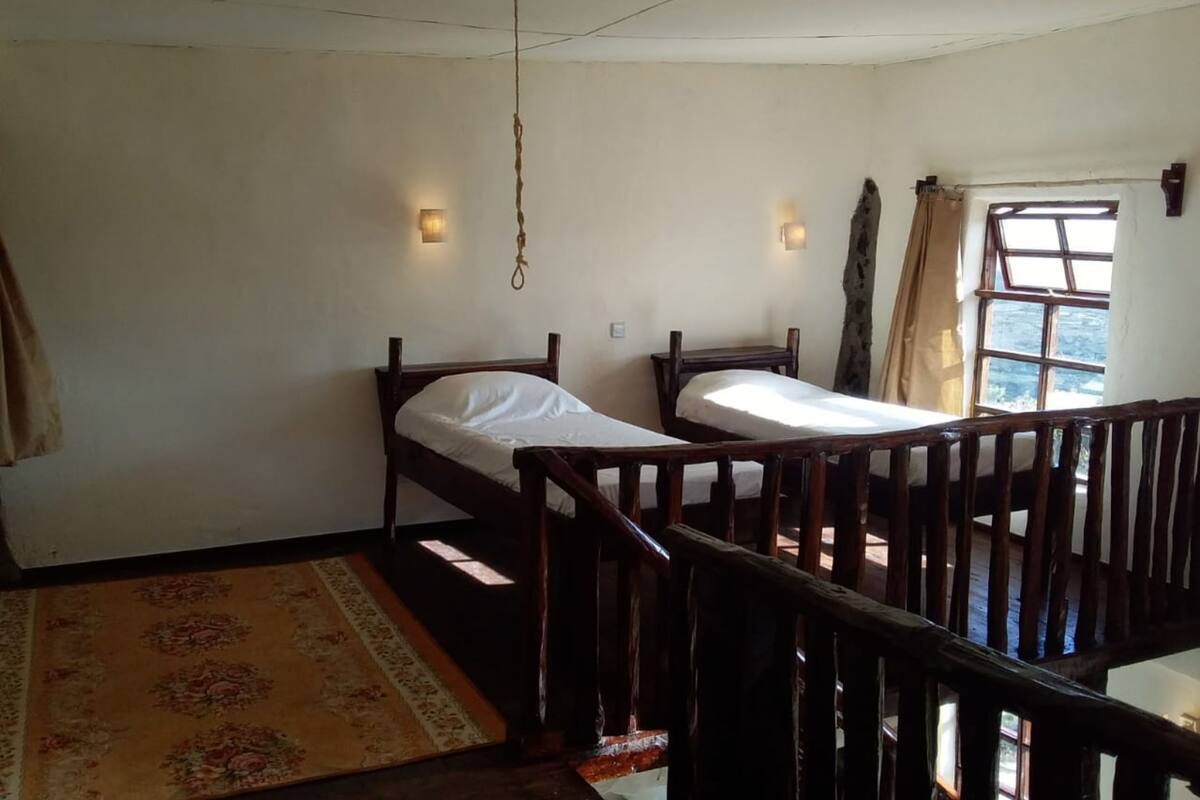 Una habitación con dos camas de madera, baranda de madera, ventana con cortinas y alfombra estampada.