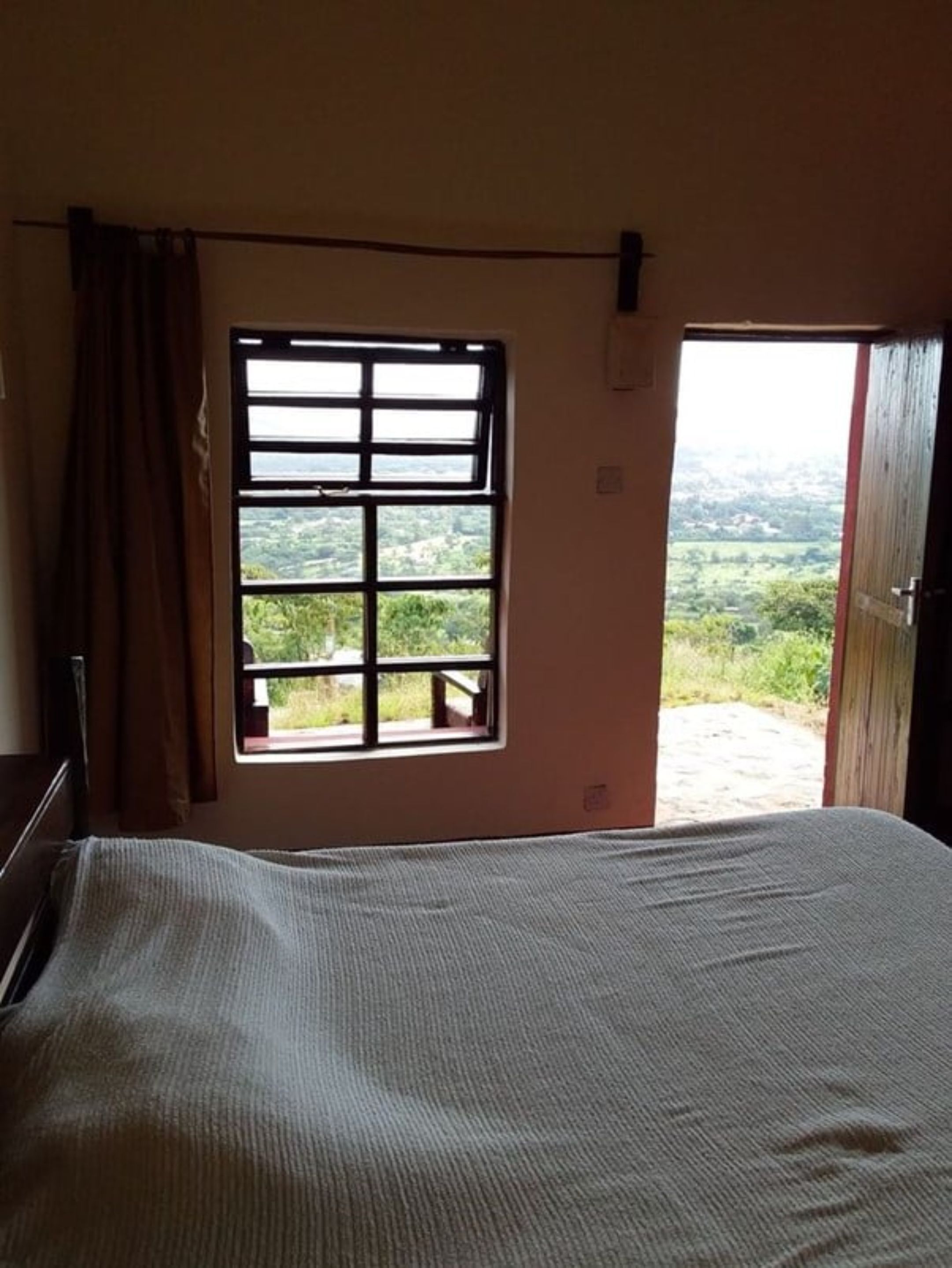 A bedroom with a large bed, a window with a view of greenery, and an open door leading outside.