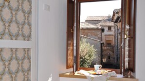 Una habitación con ventana que da a un edificio tradicional, una mesita con mantel y papel tapiz estampado.