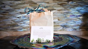 A welcome card in a paper bag with a message, placed on a decorative glass table against a stone wall. - SEE our NEW PHOTOS, One of Our BEST, (12B-2) ~ Platinum Maui Vacations (Lahaina)