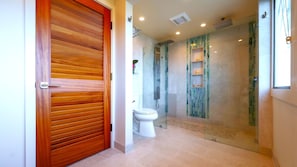 A modern bathroom with a wooden door, a glass shower enclosure, and a toilet. - SEE our NEW PHOTOS, One of Our BEST, (12B-2) ~ Platinum Maui Vacations (Lahaina)
