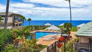 Un espace piscine agrémenté de chaises longues et de parasols, entouré de plantes tropicales et offrant une vue sur l’océan.