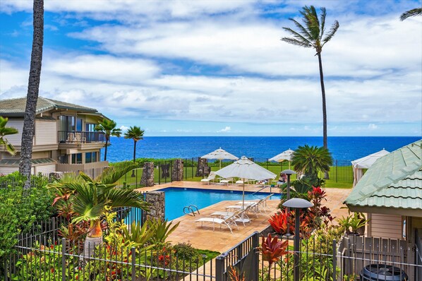 A pool area with lounge chairs and umbrellas, surrounded by tropical plants and a view of the ocean. - SEE our NEW PHOTOS, One of Our BEST, (12B-2) ~ Platinum Maui Vacations (Lahaina)