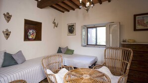 A room with two beds, wicker chairs, a window, and decorative wall pieces.