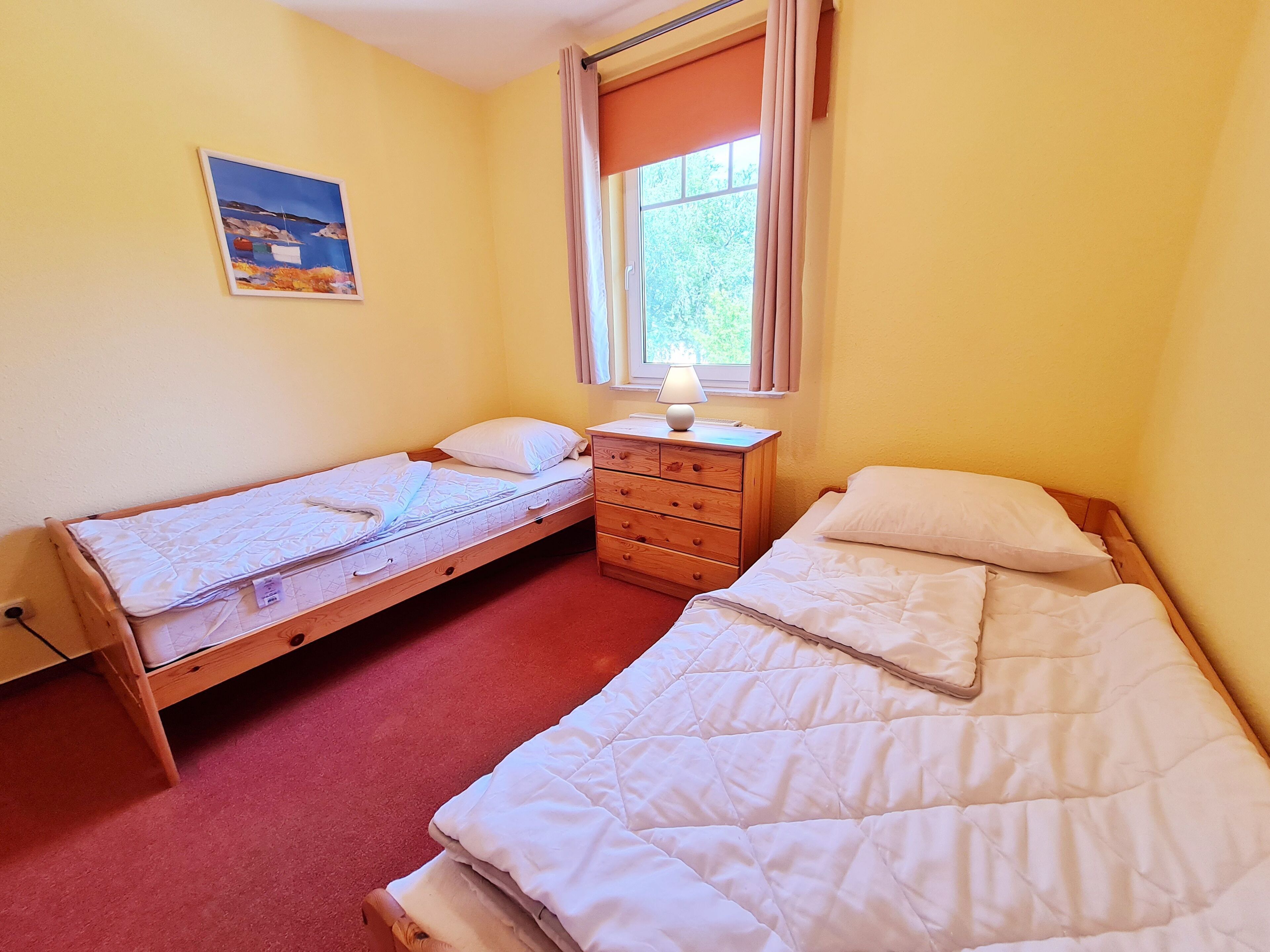 Una habitación con dos camas individuales, un aparador de madera, una lámpara y un cuadro en la pared.