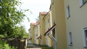 A row of yellow buildings with red roofs, a wooden fence, and green plants in the foreground. - Vacation apartment 7 Nachtigallenweg (Graal-Müritz)