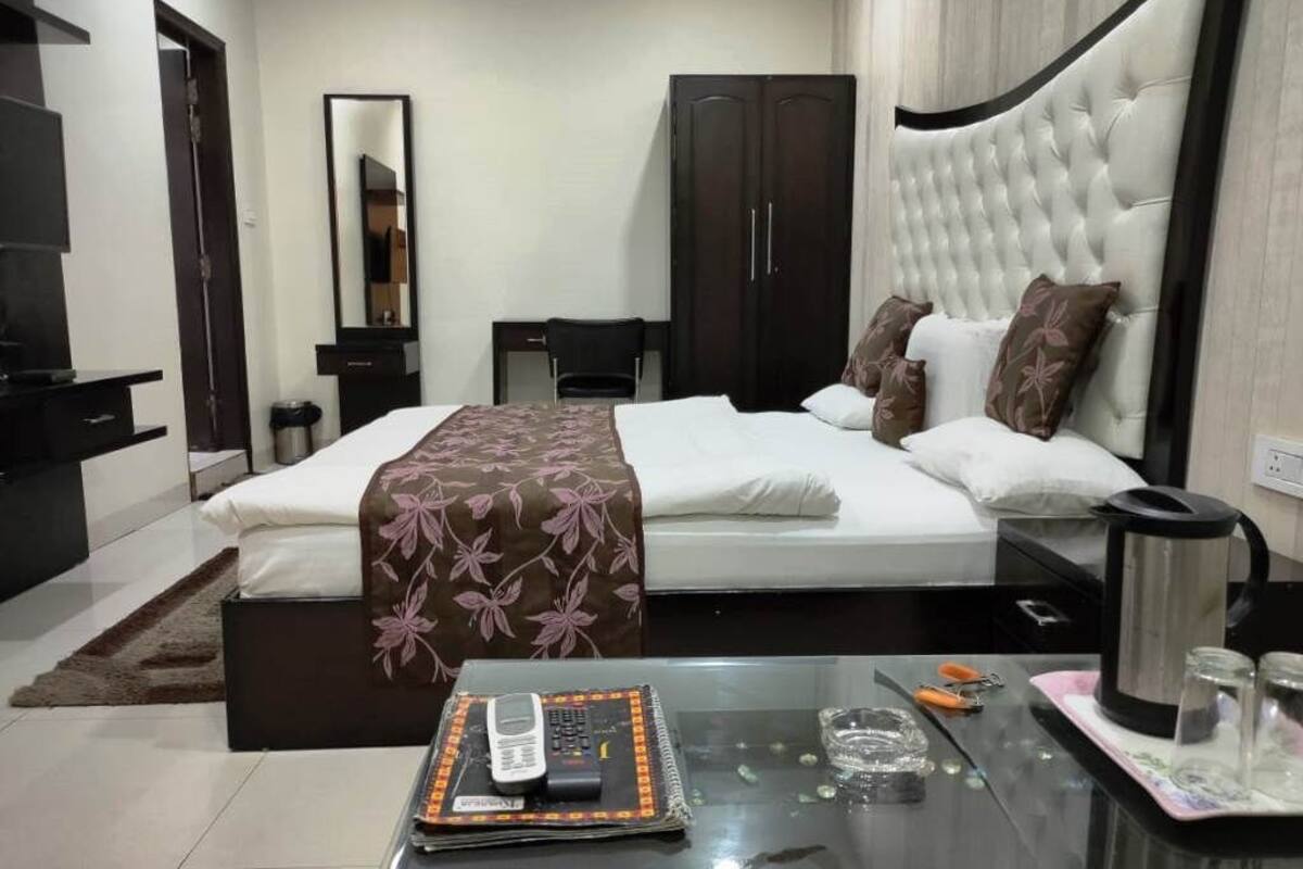 A hotel room with a bed, a bedside table with a phone, a coffee maker, and a glass of water.