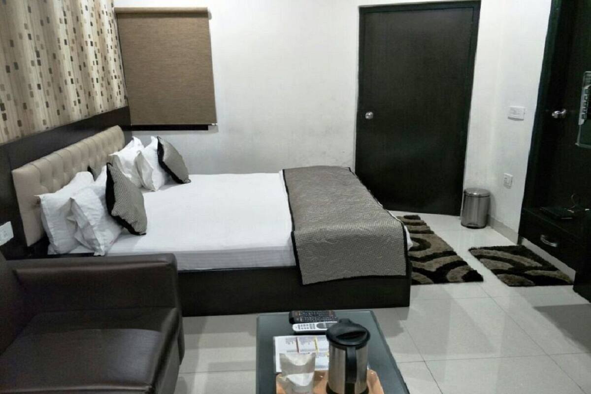 A hotel room with a bed, a sofa, a coffee table, a trash bin, and a door.
