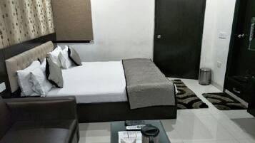 A hotel room with a bed, a sofa, a coffee table, a trash bin, and a door.