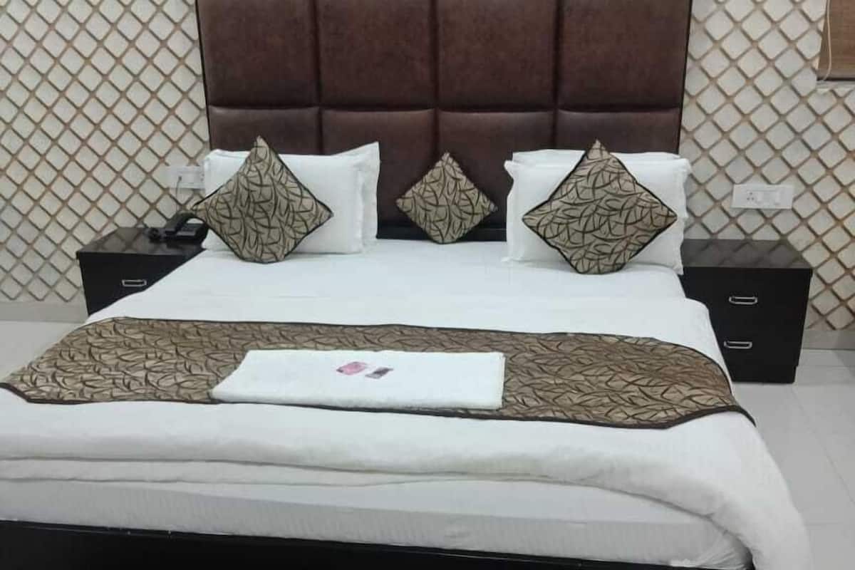 A neatly made bed with a patterned bedspread and pillows, a brown upholstered headboard, and a patterned rug on the floor.
