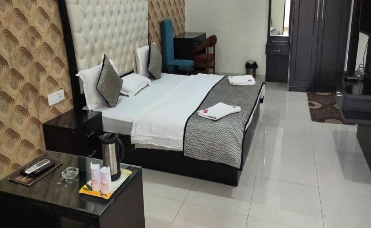 A hotel room with a bed, a desk with a kettle, a chair, and a wardrobe.