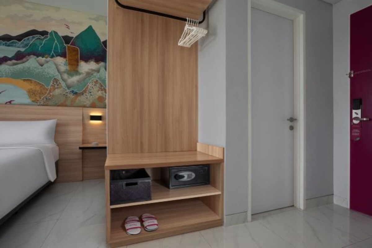 A hotel room with a bed, a wooden shelf with shoes, a door, and a wall painting.
