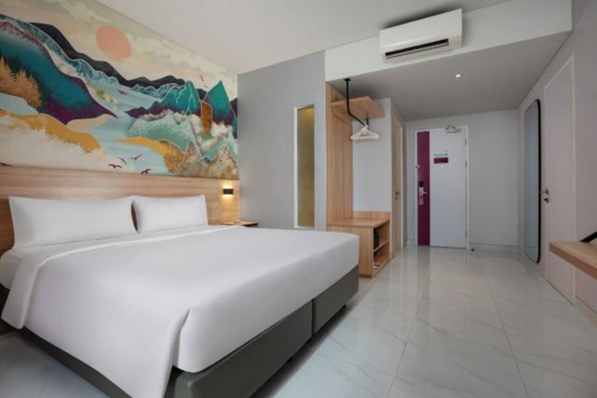 A hotel room with a large bed, a mural on the wall, a desk, and a door.