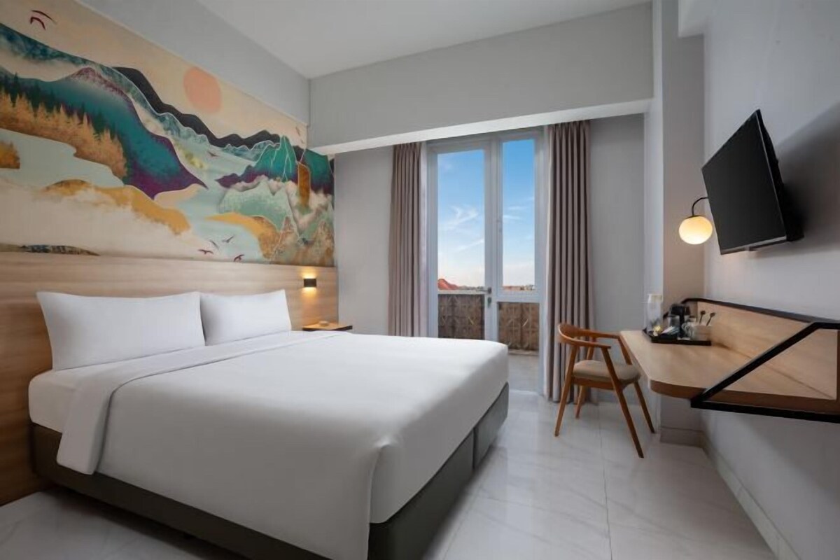 A hotel room with a bed, a desk, a chair, a TV, and a large window.