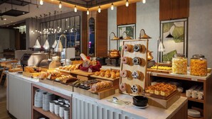 A buffet with various baked goods, a coffee machine, and a display of donuts. - fave+ hotel Pamanukan (Pamanukan)