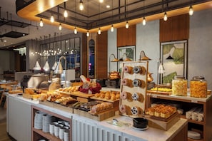 A buffet with various baked goods, a coffee machine, and a display of donuts.